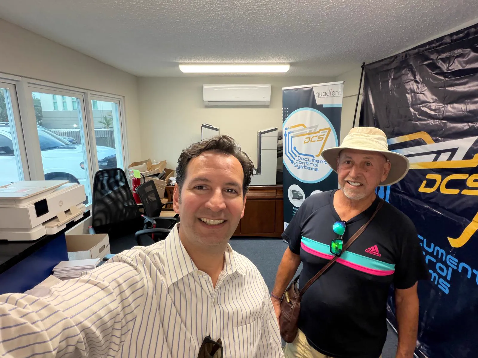 Two visitors smiling at the DCS offices in front of company banners